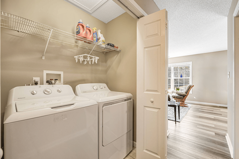A laundry room with a washer and dryer and a chair in the background.