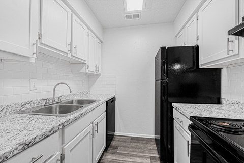 A black refrigerator stands in a kitchen with white cabinets and a marble countertop.