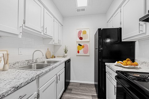 A black refrigerator sits in a kitchen with white cabinets and a marble countertop.