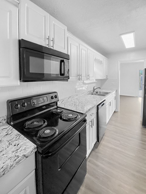 A black and white photo of a kitchen with a stove, microwave, and cabinets.