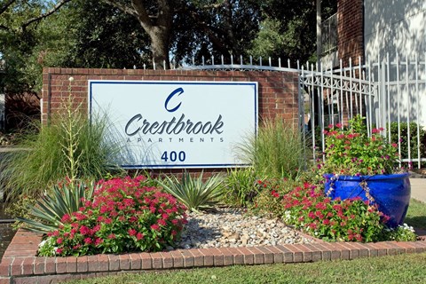 A sign for Crestbrook Apartments is surrounded by flowers and plants.