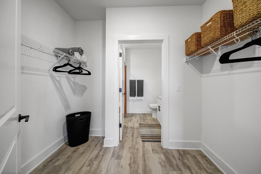 a bathroom with white walls and wood flooring and a closet with shelves and baskets