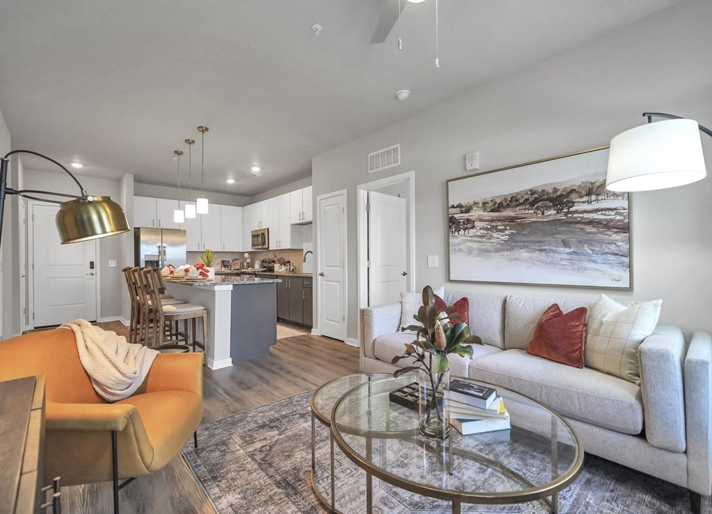 a living room with a couch table and chairs and a kitchen in the background