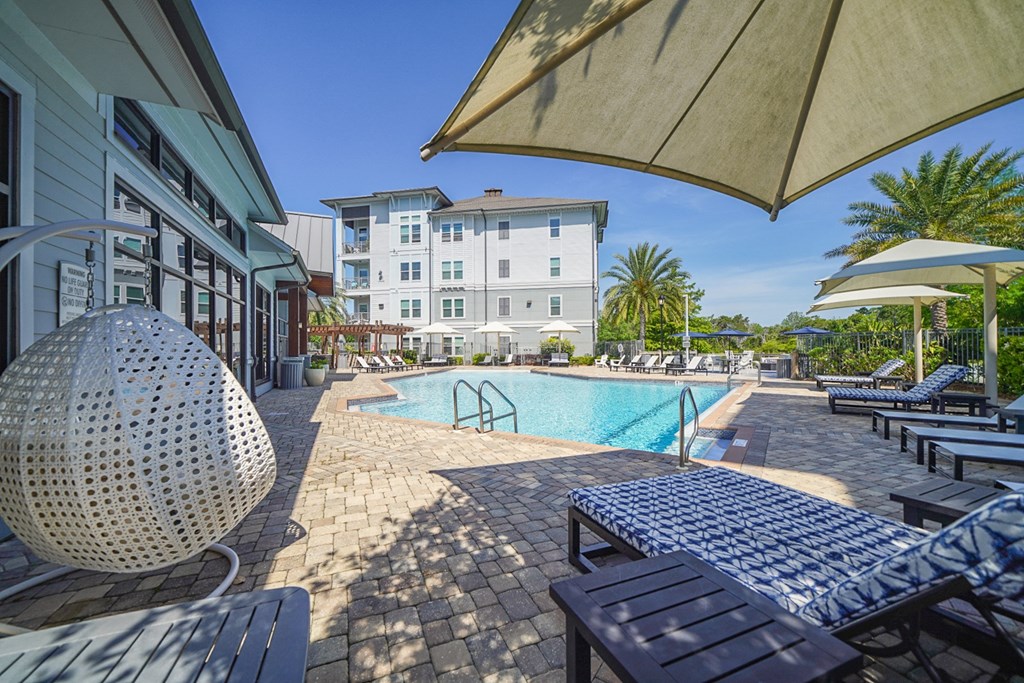 a swimming pool with lounge chairs and umbrellas in front of a building
