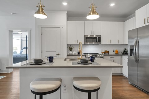 a kitchen with white cabinets and a large island with two stools at The Indigo Apartments, Canton, GA, 30114