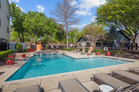 A pool surrounded by trees and lounge chairs.