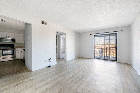 A spacious room with wooden flooring and a sliding glass door leading to a balcony.