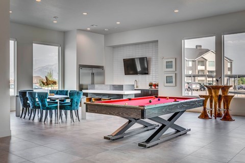 A pool table is in the middle of a room with blue chairs and a television.
