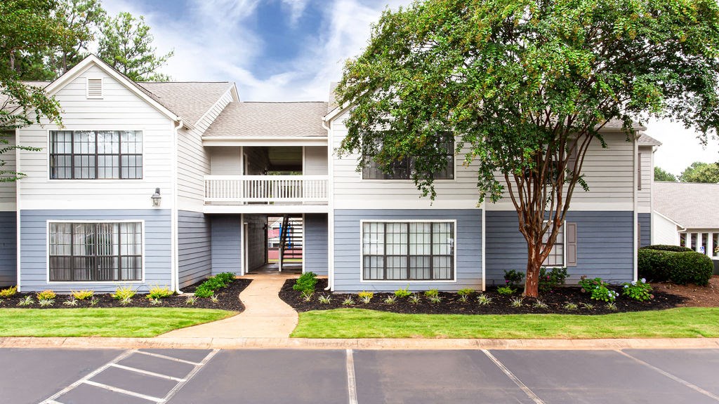 a white and blue house with a tree in front of it at Magnolia Place at Stockbridge Apartments, Stockbridge, Georgia