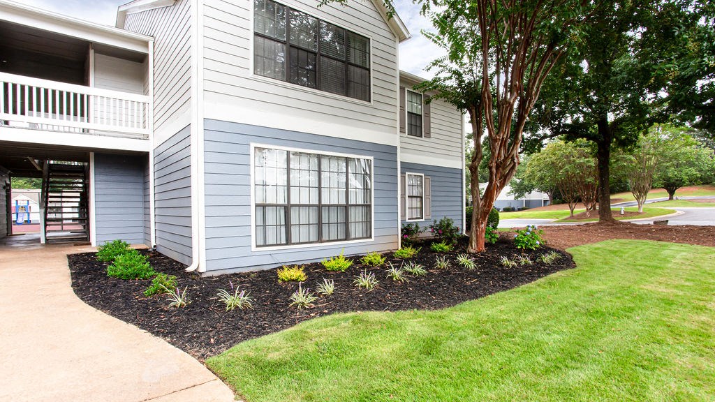 a front yard with a tree and a blue house at Magnolia Place at Stockbridge Apartments, Georgia, 30281