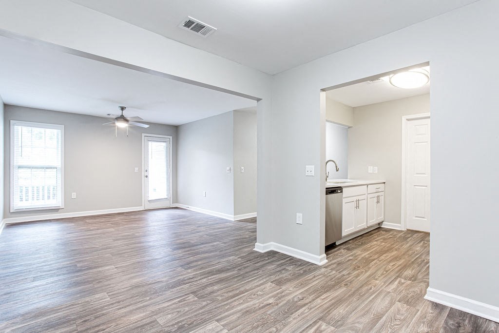 an empty living room with a kitchen and a ceiling fan with window at Magnolia Place at Stockbridge Apartments, Stockbridge, GA