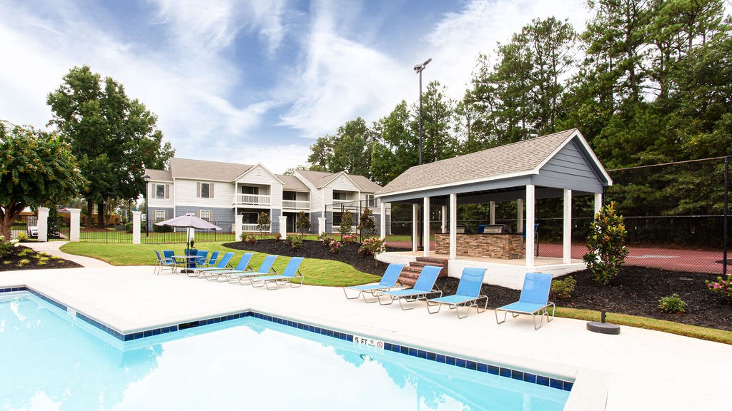 a swimming pool with blue lounge chairs in front of a house at Magnolia Place at Stockbridge Apartments, Stockbridge, GA, 30281