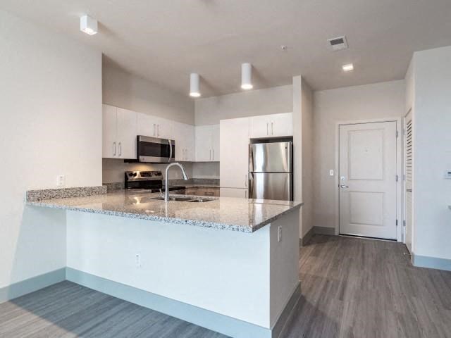 A kitchen with a breakfast bar, granite countertops, hardwood style flooring, and access to the front door at Lofts at South Lake, Clermont, 34711