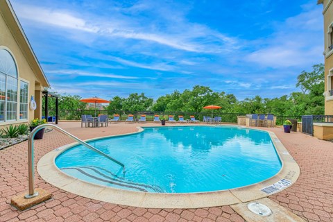 A swimming pool surrounded by a brick patio and a building in the background.
