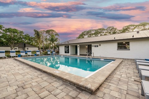 A swimming pool surrounded by a brick patio and a white building.
