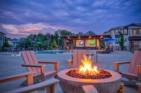 A fire pit in the middle of a patio with chairs around it.