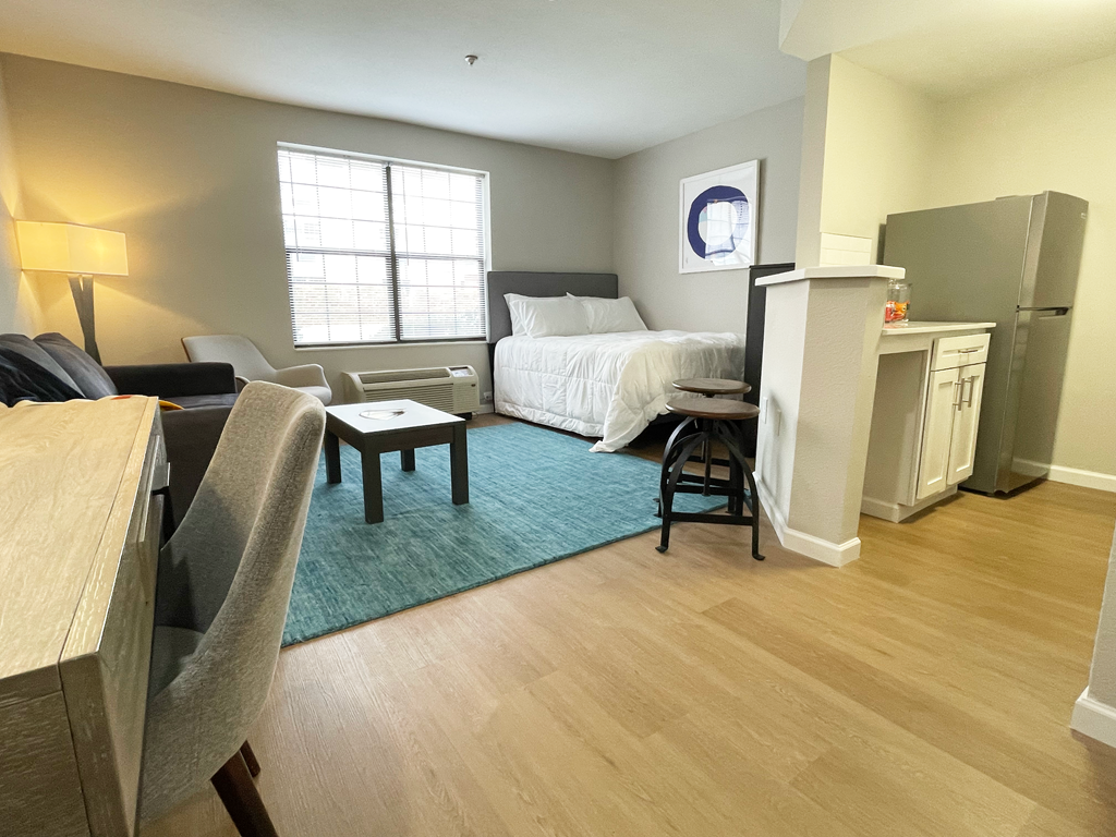 a bedroom with a bed and a living room with a desk and chairs