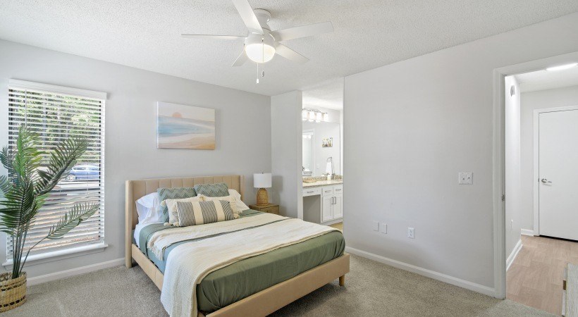 A bedroom with a bed, a ceiling fan, and a painting on the wall.