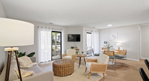 A living room with a grey sofa, a wicker ottoman, a wooden coffee table, and a television mounted on the wall.