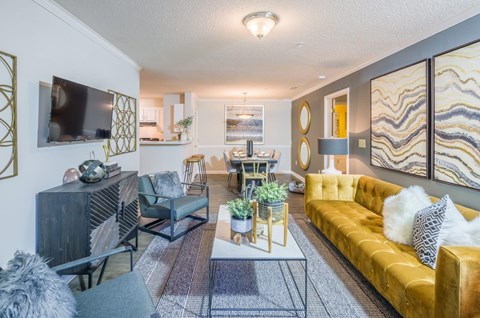 A living room with a yellow couch and a television on the wall.