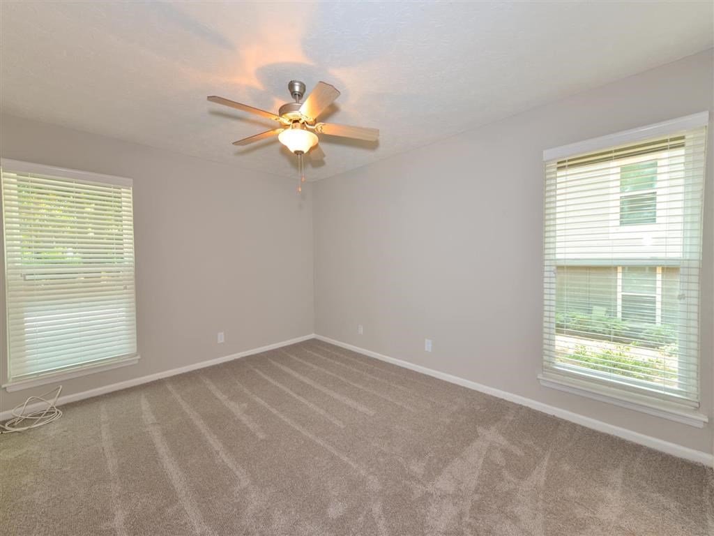 an empty bedroom with a ceiling fan and two windows