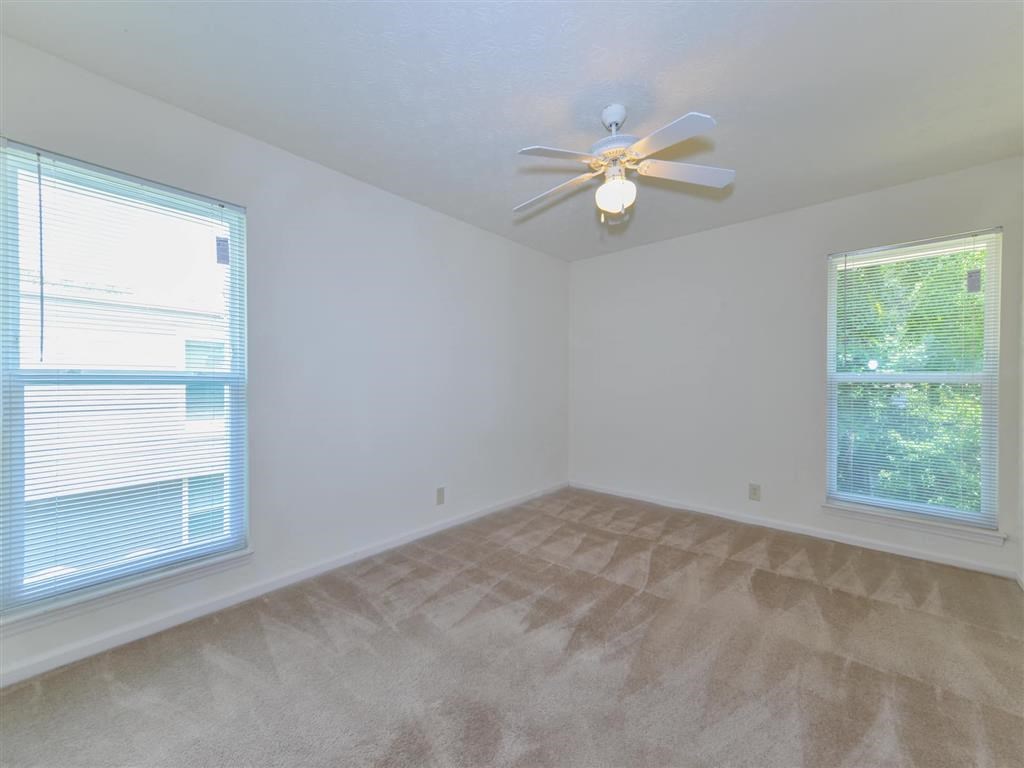 an empty living room with a ceiling fan and two windows
