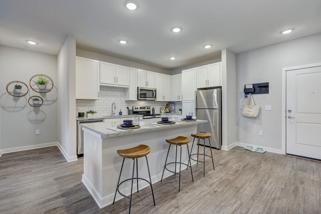 a kitchen with a large island with three stools at Century Mundy Mill Apartments, Oakwood, GA