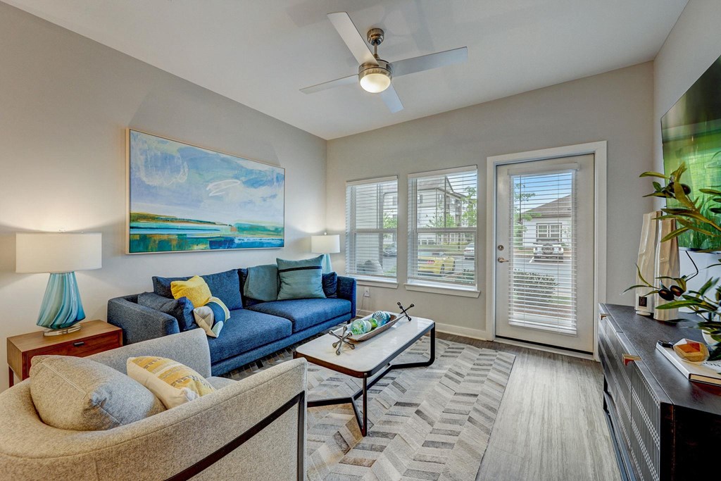 a living room with a blue couch and a ceiling fan at Century Mundy Mill Apartments, Oakwood 30566