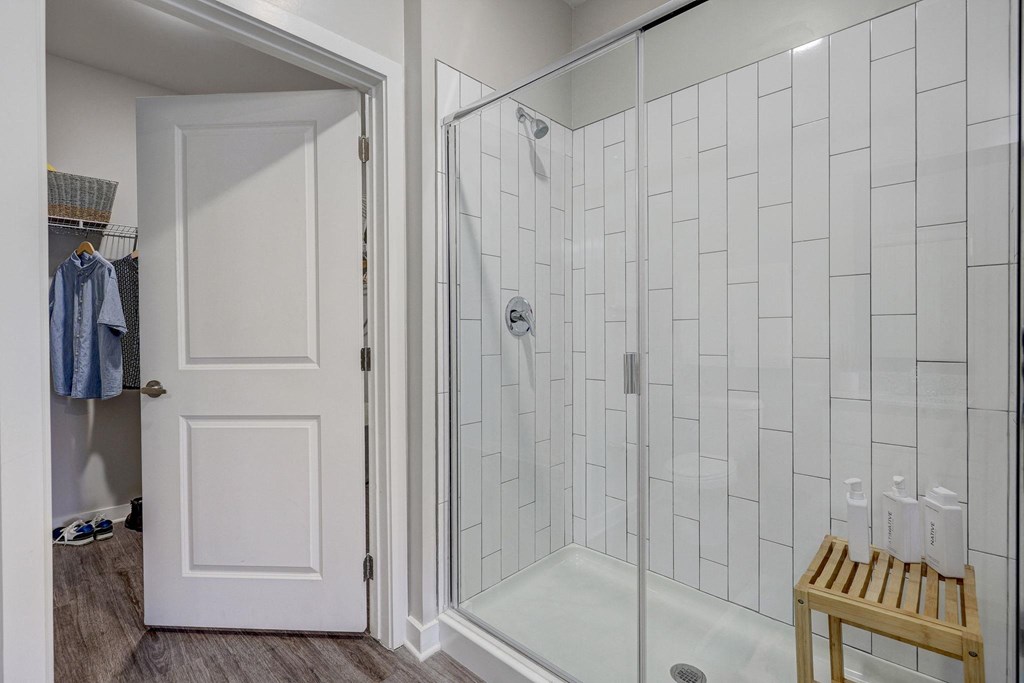 a shower with a glass door in a white tiled bathroom at Century Mundy Mill Apartments, Oakwood, GA 30566