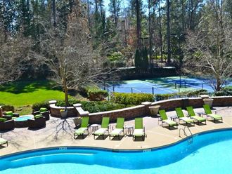 a swimming pool with chaise lounge chairs and a tennis court in the background at Flats at North Springs, Sandy Springs, GA 30328