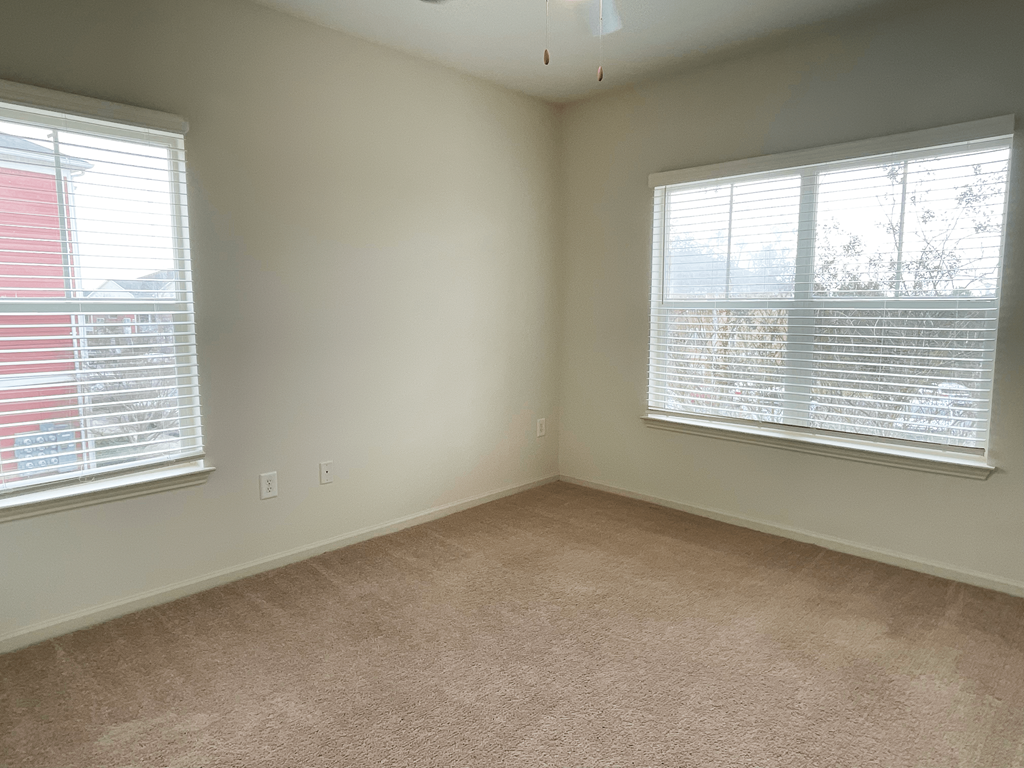an empty living room with two windows and carpet