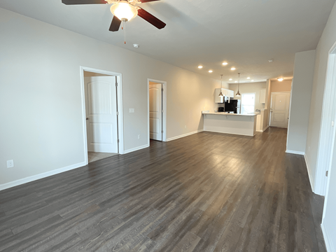 an empty living room with a ceiling fan and a kitchen