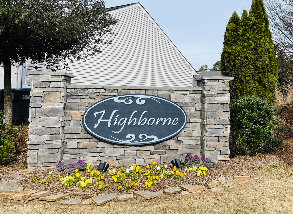 a sign on a stone wall with flowers in front of a house