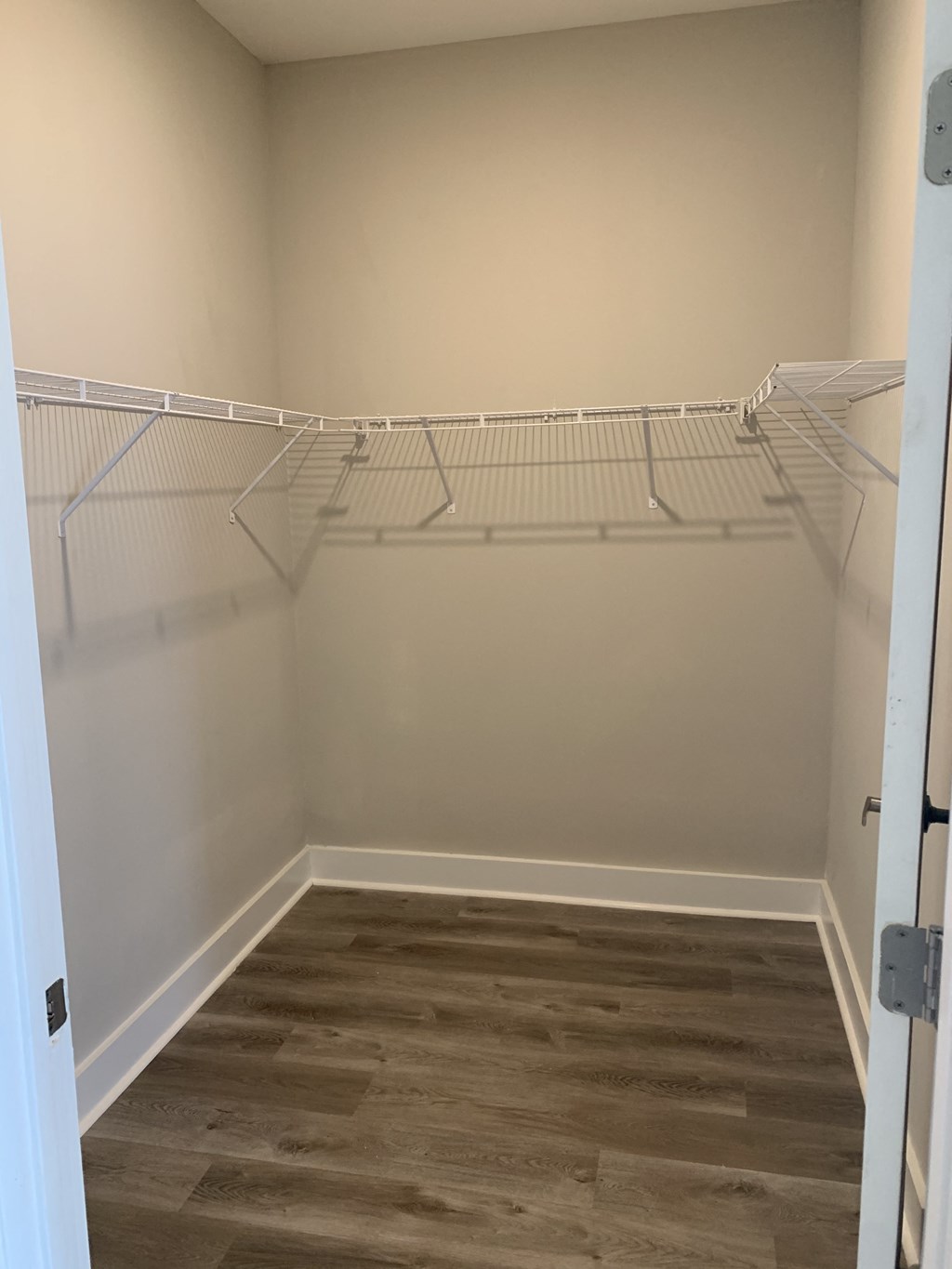 a walk in closet with white shelves and a wood floor