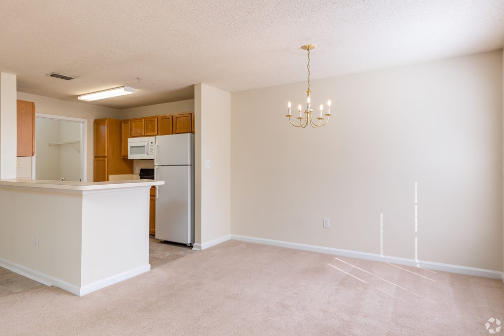 an empty living room with a kitchen and a refrigerator