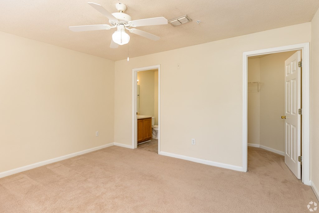an empty living room with a ceiling fan and a door to a bathroom
