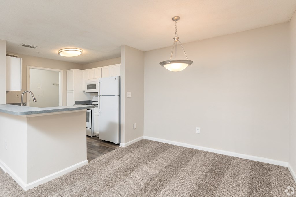 an empty living room with a kitchen with a white refrigerator and a counter top