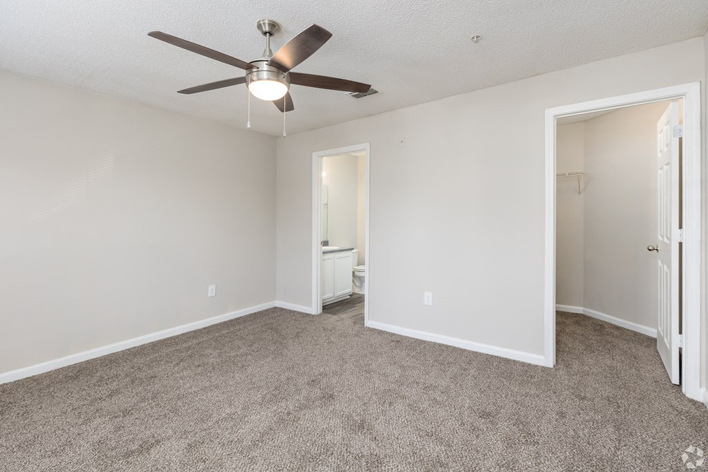 an empty living room with a ceiling fan and a door to a bathroom