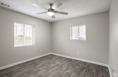 A room with a ceiling fan and two windows.