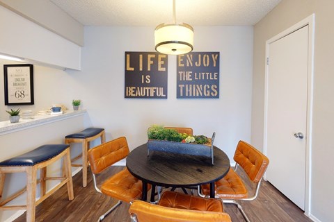 A dining room with a table and chairs and a sign on the wall that says "LIFE ENJOY THE LITTLE BEAUTIFUL THINGS".