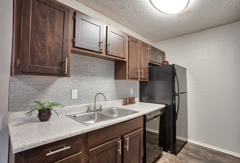 A kitchen with a black refrigerator and wooden cabinets.