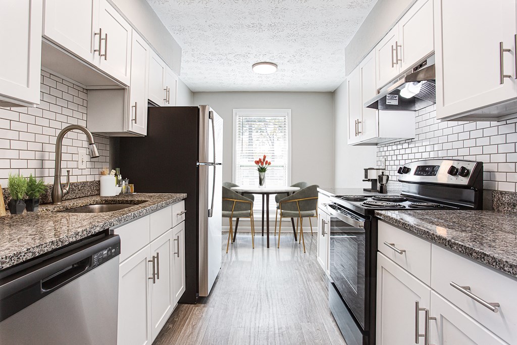 a kitchen with white cabinets and black appliances and a table with chairs at The Ellis Apartments, Georgia
