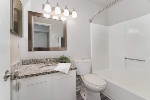 A white bathroom with a granite countertop and a white toilet.
