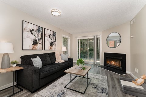 A modern living room with a black couch, a fireplace, and a painting on the wall.