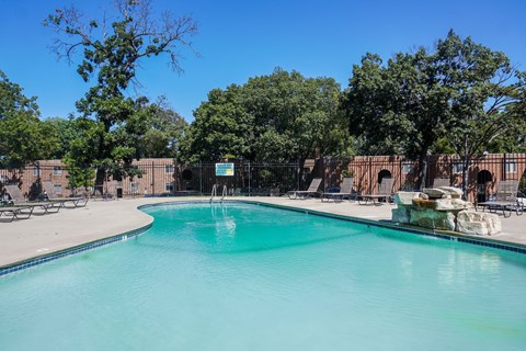 A swimming pool surrounded by trees and chairs.