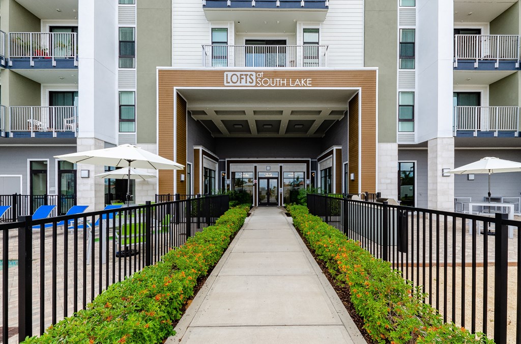 an apartment building with a sidewalk and a fenced in area with umbrellas at Lofts at South Lake, Clermont, 34711