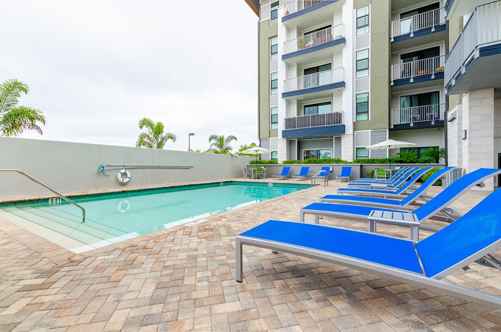 a swimming pool with blue lounge chairs in front of an apartment building at Lofts at South Lake, Florida
