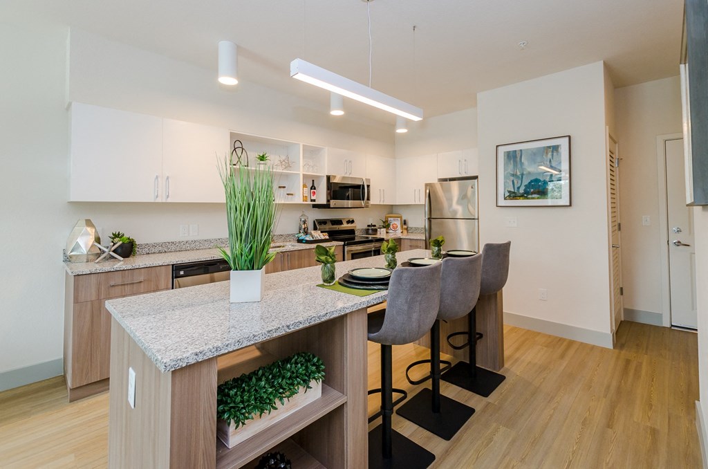 an open kitchen and dining area with a granite counter top and a bar with chairs at Lofts at South Lake, Clermont, 34711