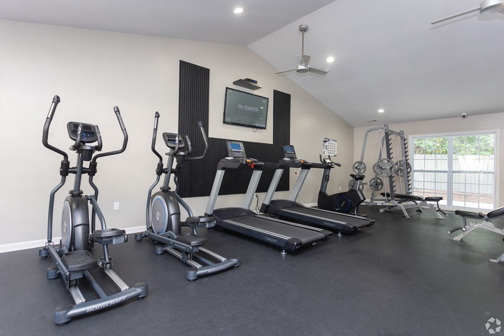 a gym with treadmills and weights and a tv on the wall
