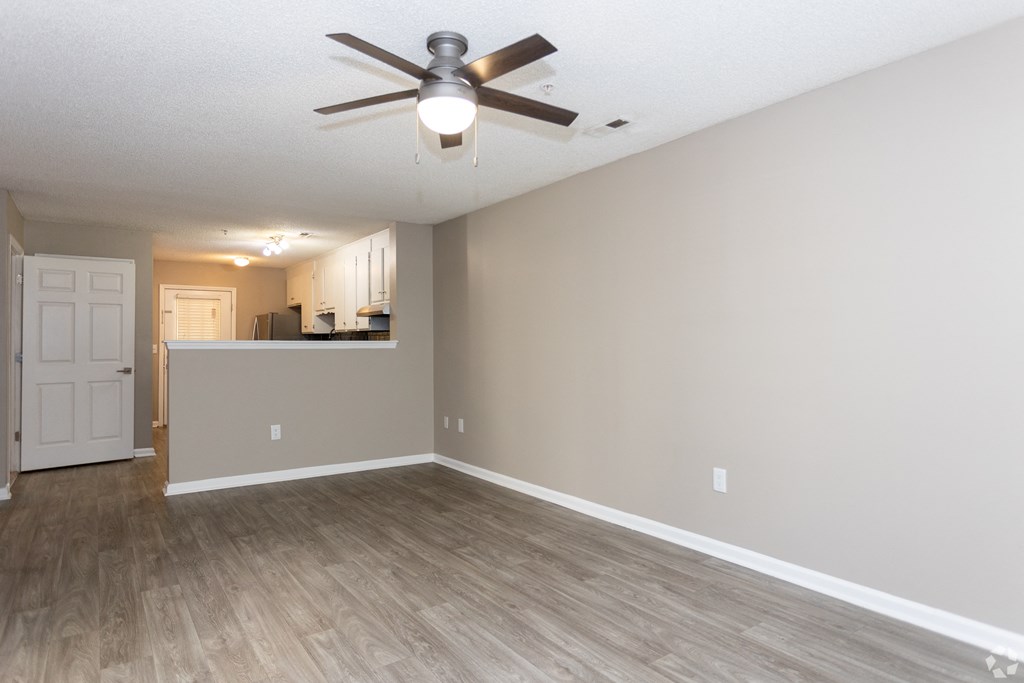 an empty living room with a ceiling fan and a kitchen